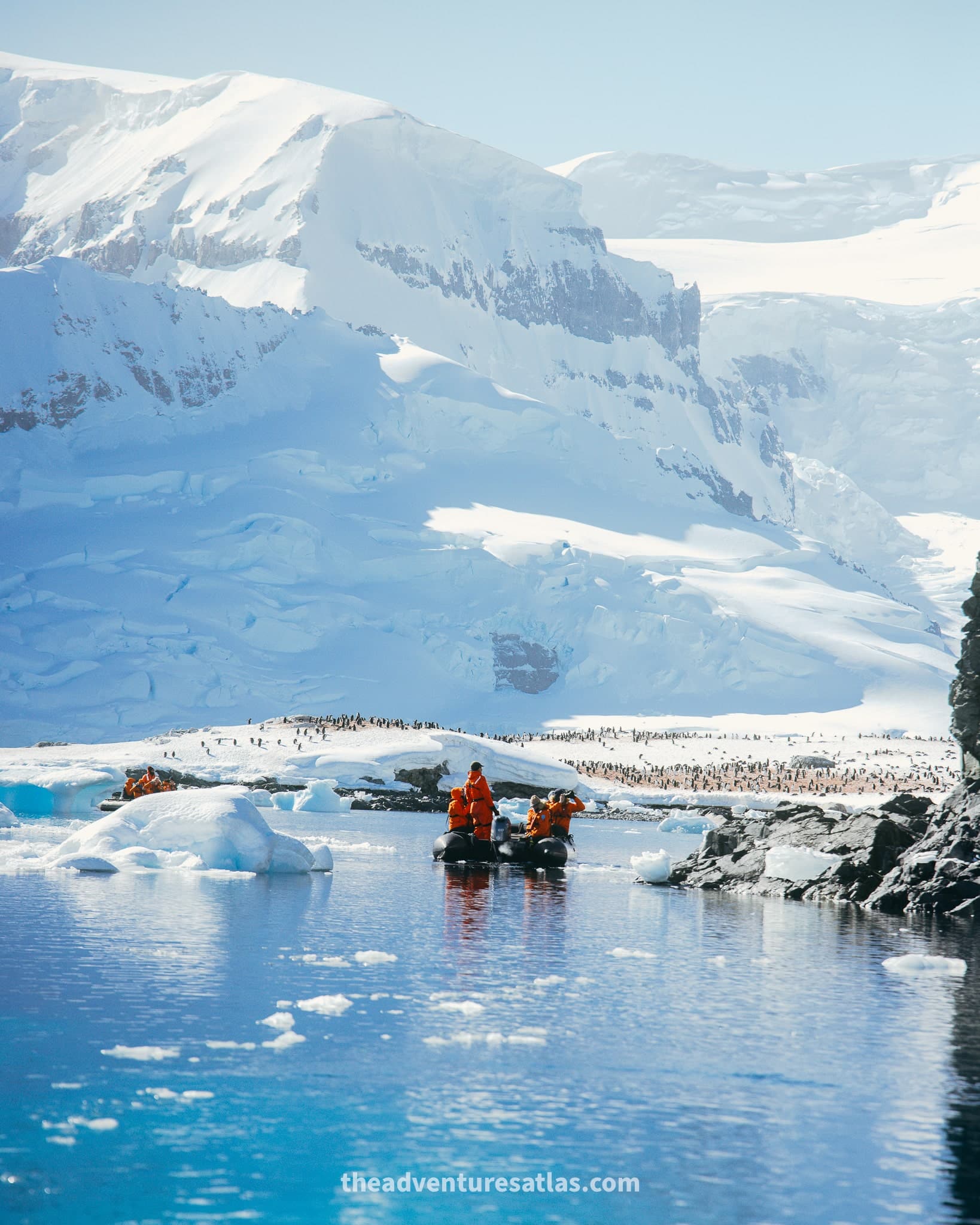 A Zodiac boat full of passengers in orange parkas watching a massive colony of penguins in on the Antarctica peninsula
