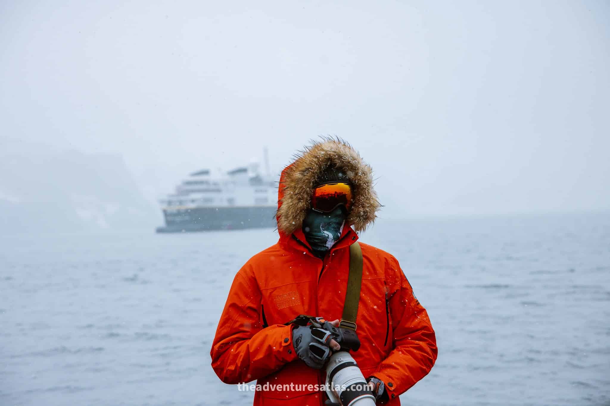 Photographer standing in front of an Antarctica expedition ship wearing a parka, ski goggles and gloves