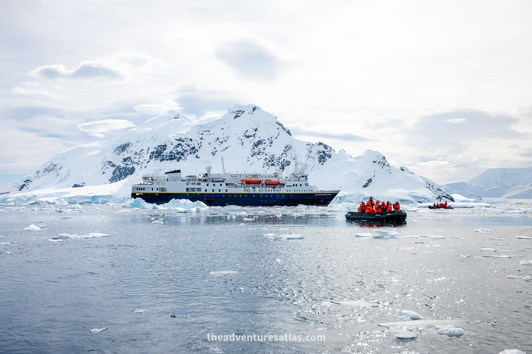 The National Geographic Explorer ship and zodiac with passengers sailing through a calm Antarctic bay surrounded by snow-covered mountains