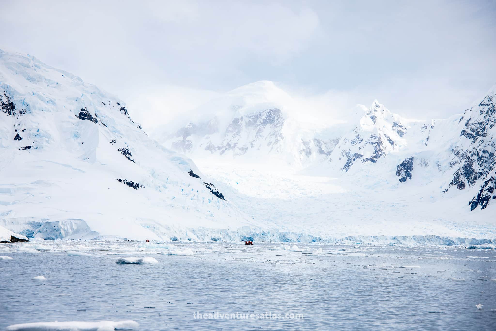 A tiny zodiac cruises past enormous mountains in Antarctica