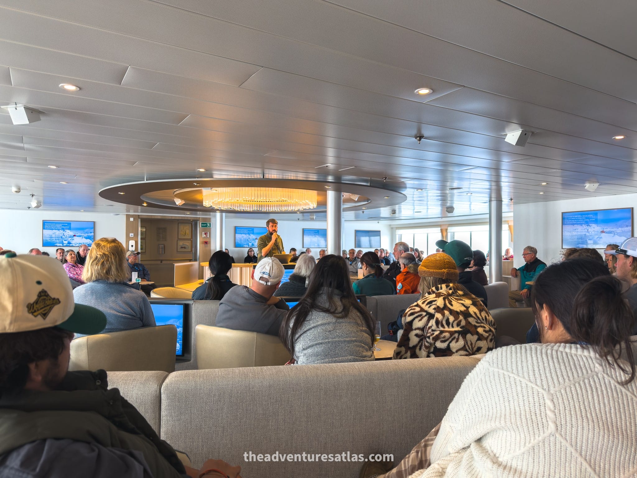 A group of passengers listening to a lecture from an expert guide in the main lounge of an expedition ship on a cruise to Antarctica
