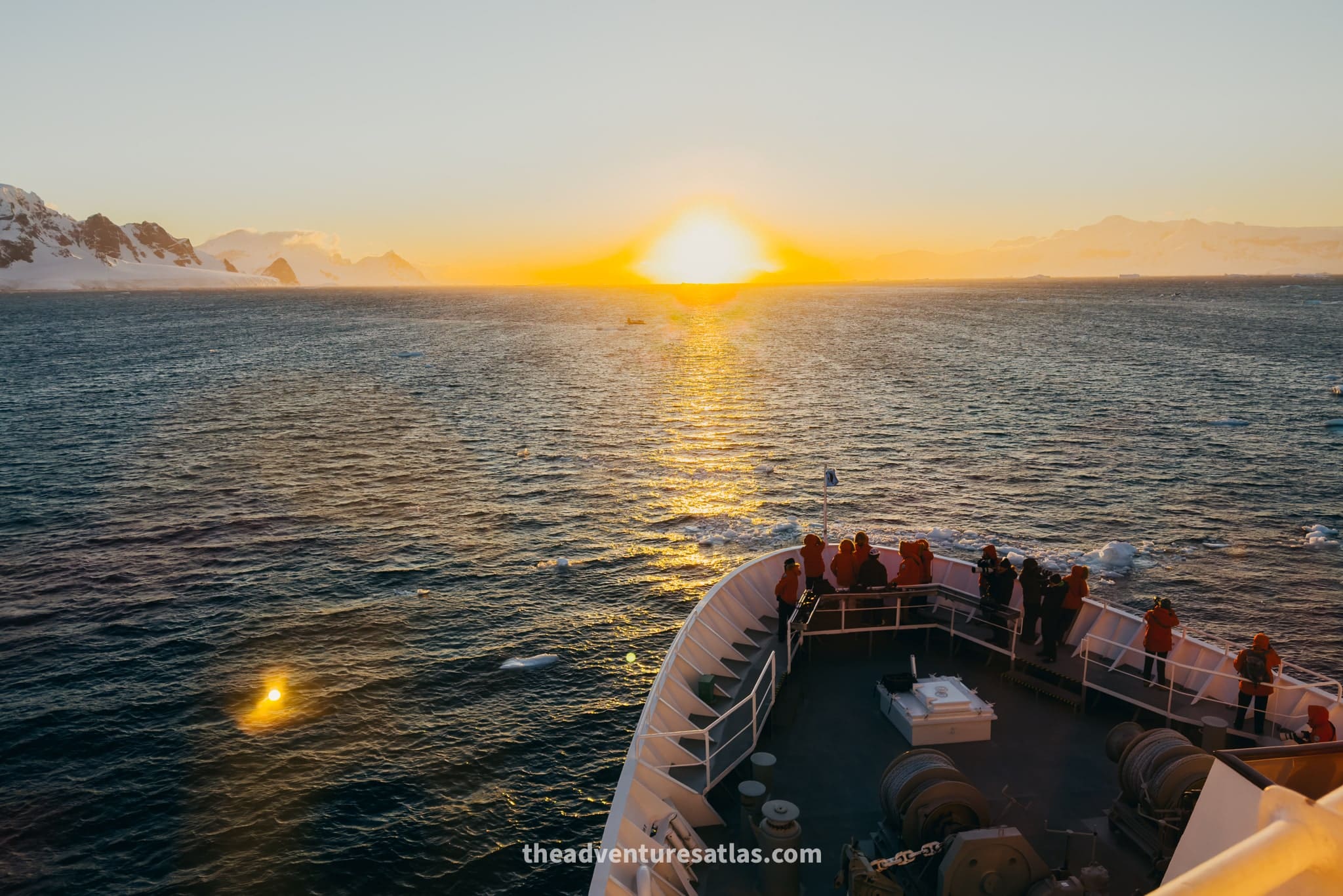 A vibrant, fiery orange and pink sunset exploding in the sky over the icy Lemaire Channel in Antarctica