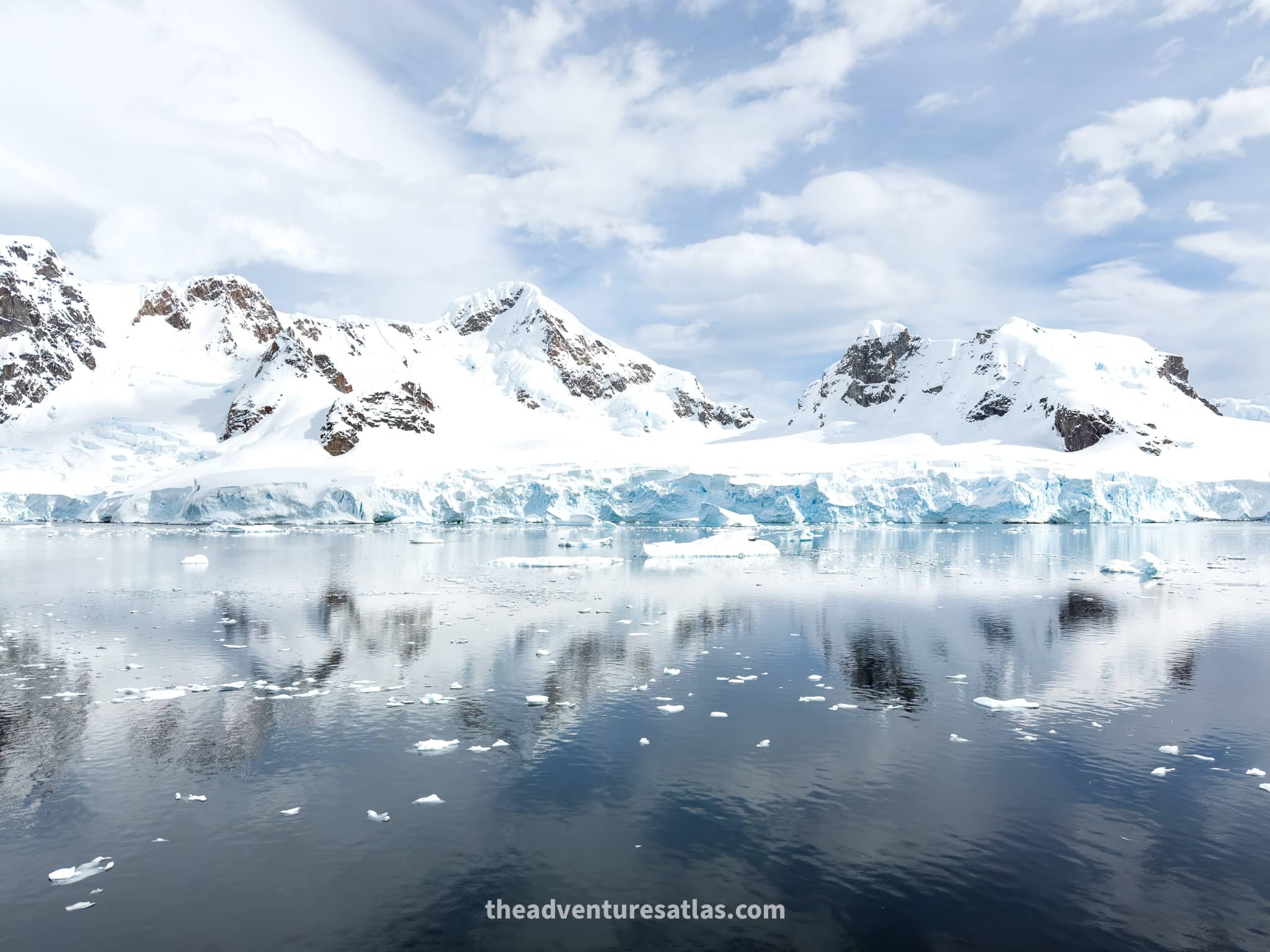 A stunning landscape of Paradise Bay on a sunny day, with snow-covered mountains reflecting perfectly in the calm, blue water.