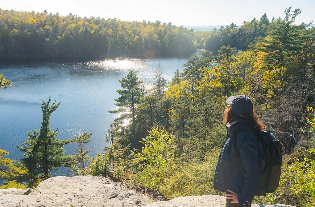 A woman hiking along the edge of a viewpoint of the lake and forest in Minnewaska State Park in Ulster County NY on a spring day